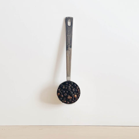 Close up of black peppercorns on a metal scoop
